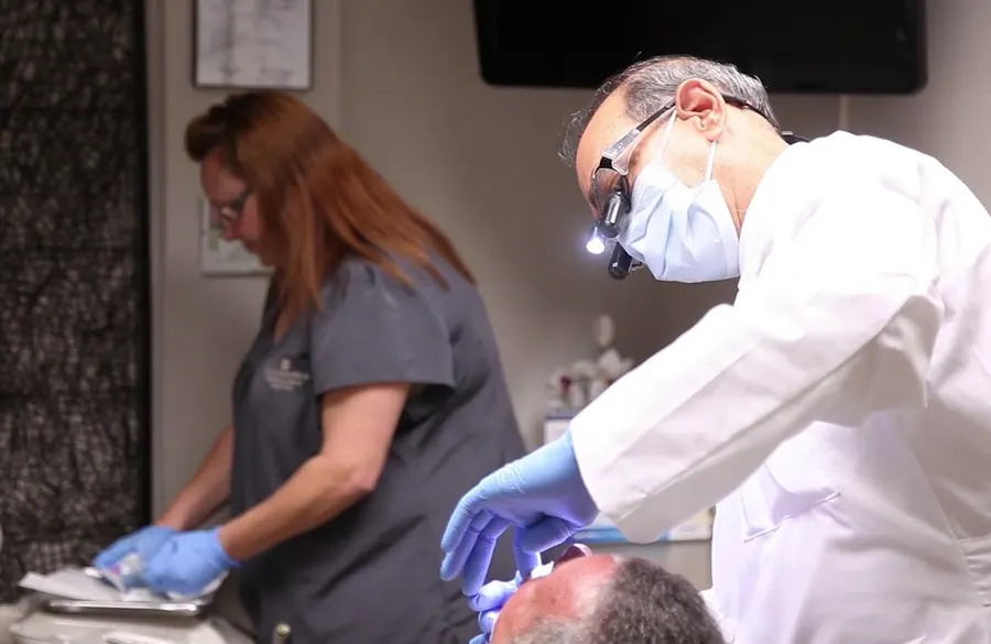 Dr. Chenet treating a patient, with a dental assistant beside him.
